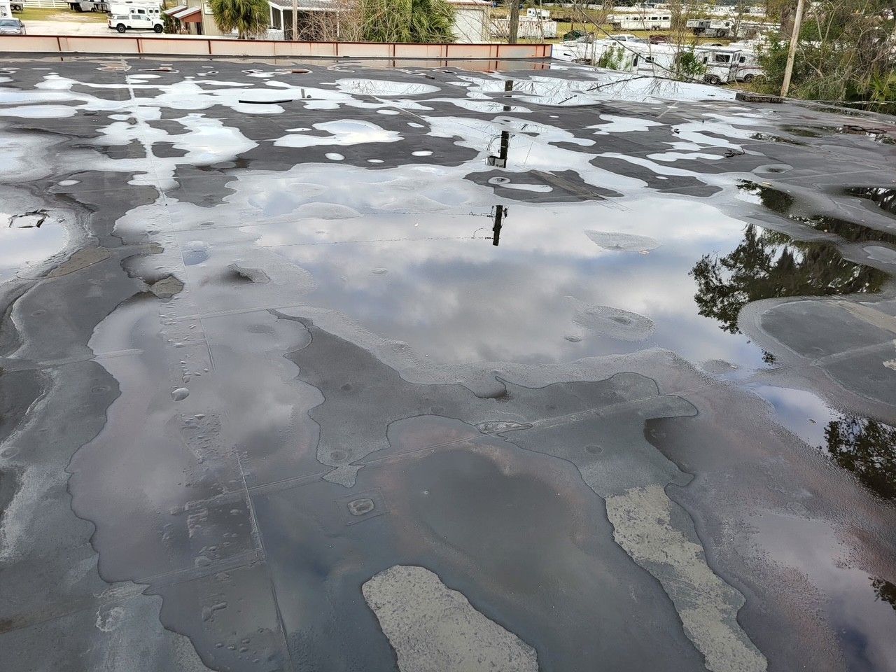 Wet black rooftop with puddles reflecting the sky and trees