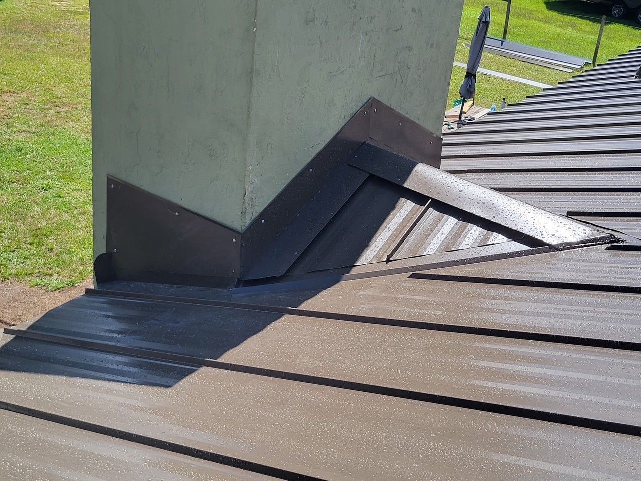 Rooftop around a concrete chimney with black flashing and brown metal panels