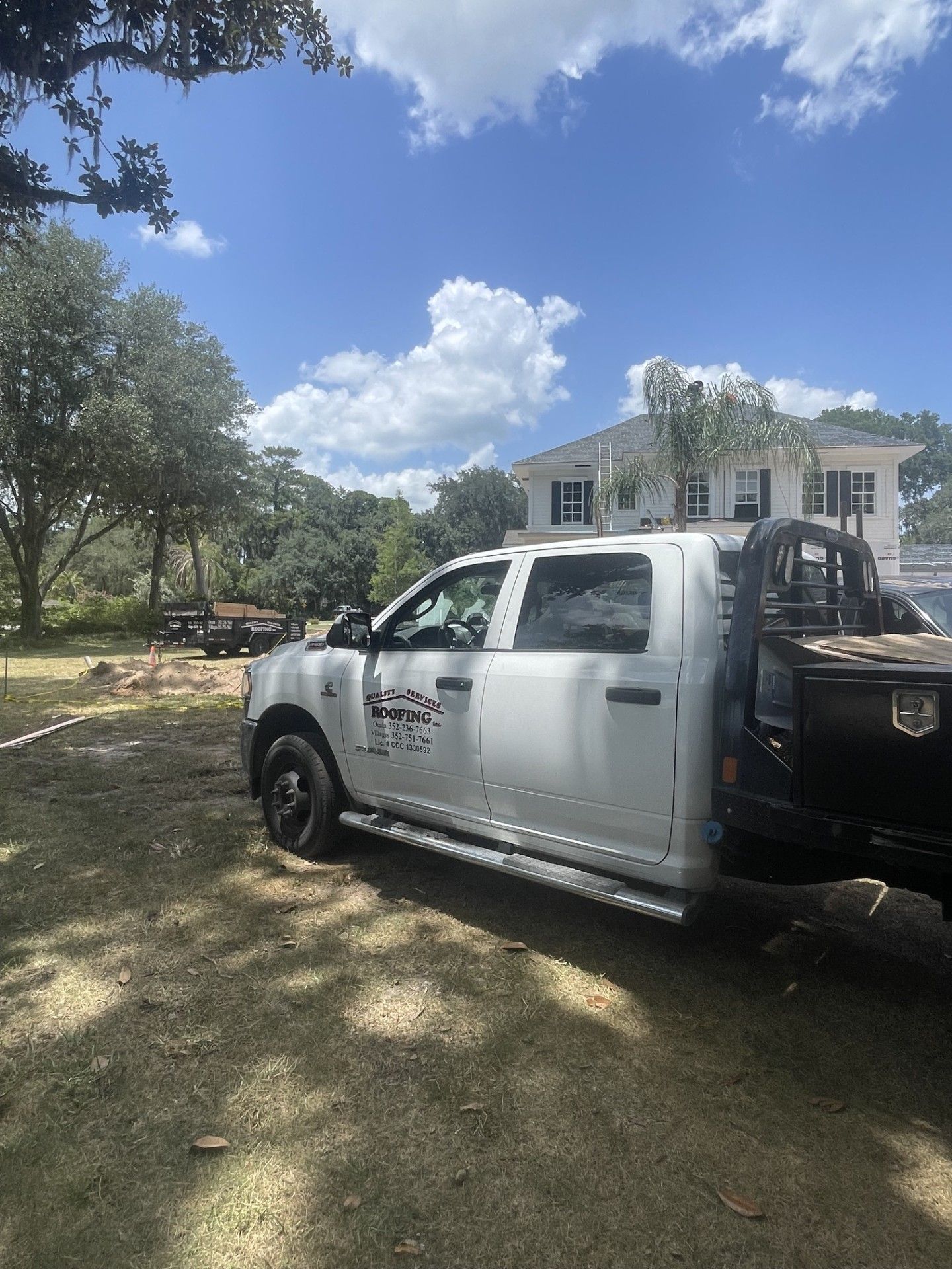 White pickup truck parked on grass beside a house with trees and blue sky overhead
