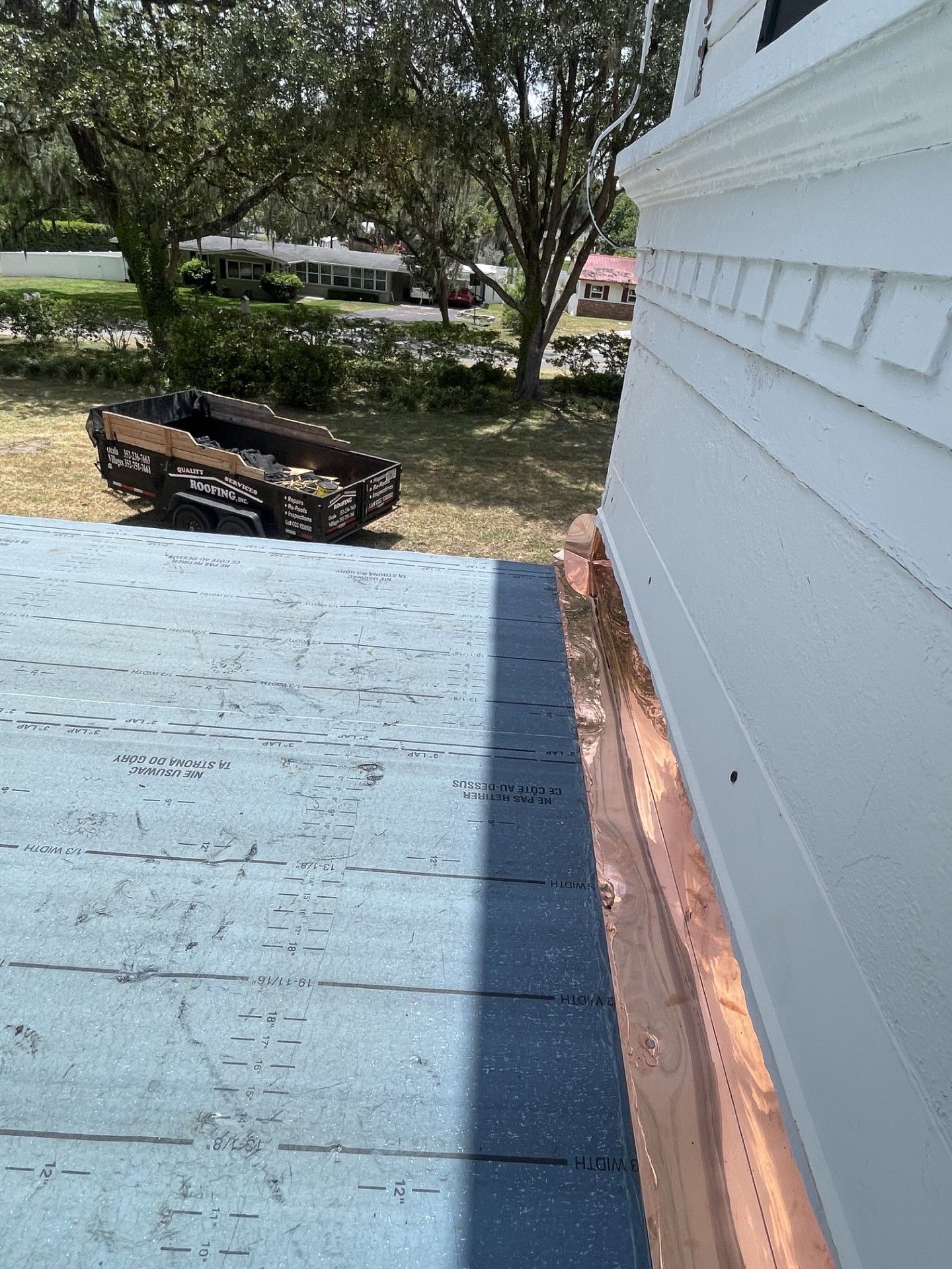 White house siding beside a blue porch roof, with trees and a bench in the yard.