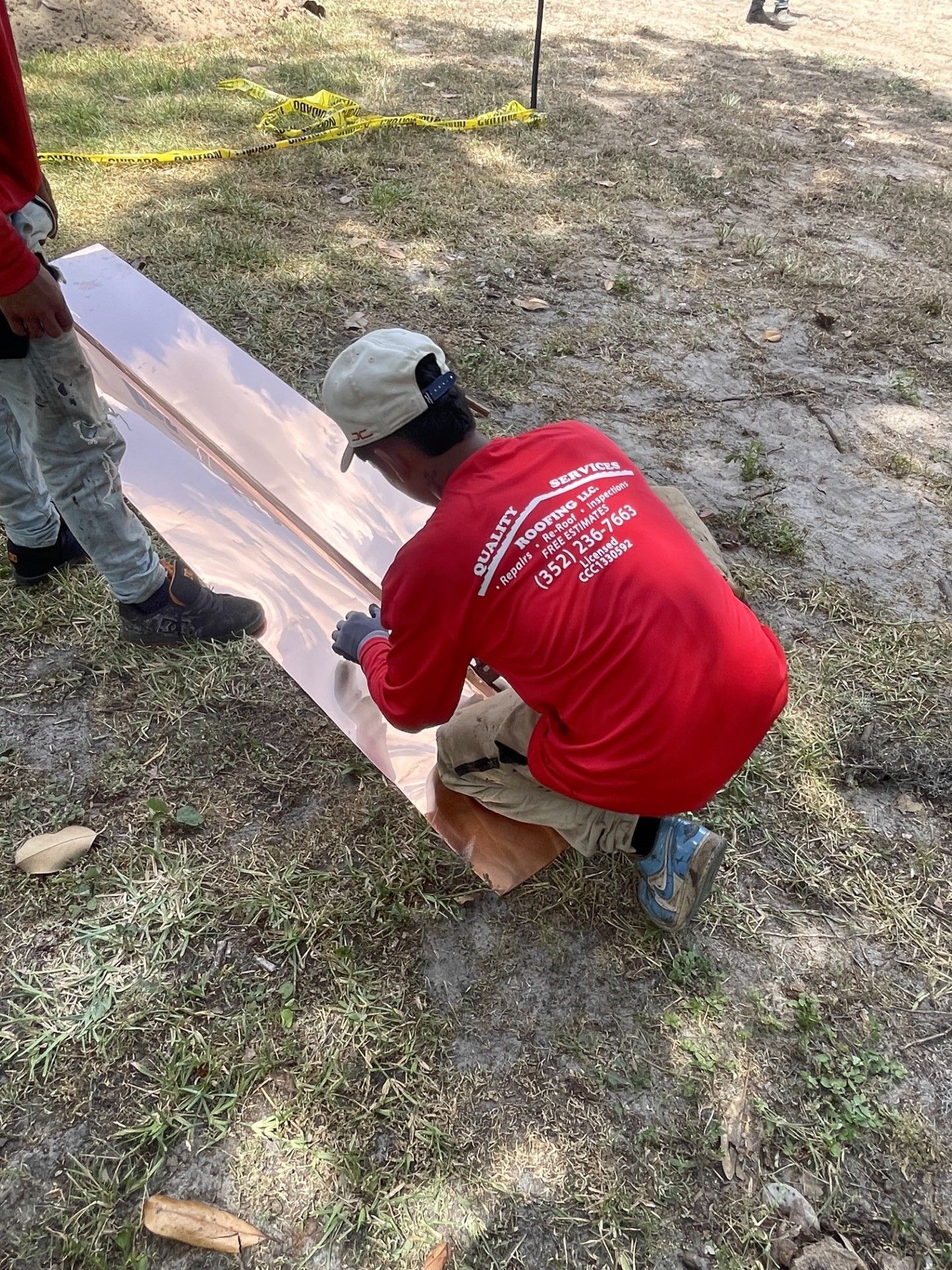 Person in a red shirt crouches beside a long white board outdoors, measuring or marking it.