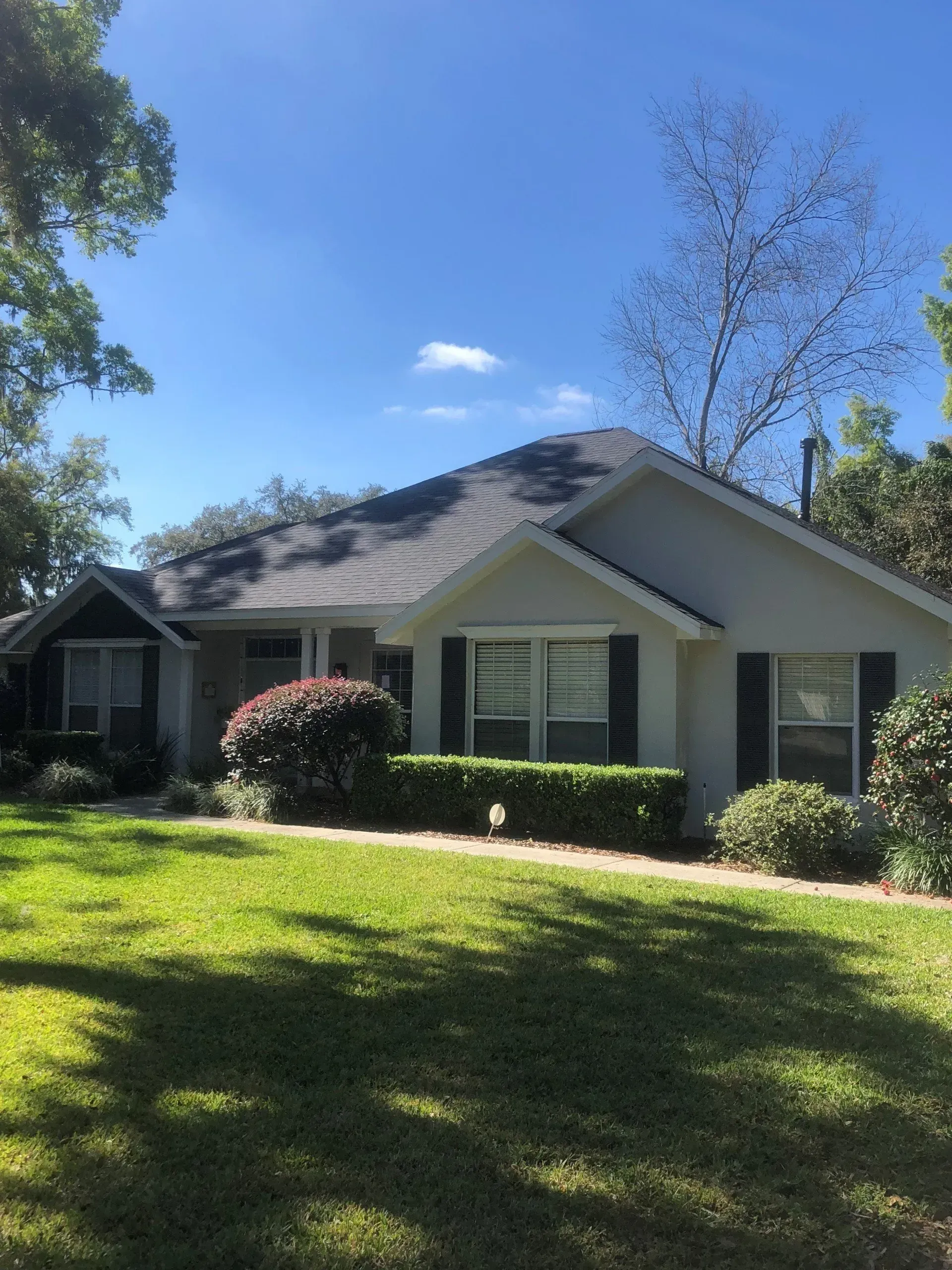 Suburban house with gray roof, white siding, trimmed hedges, and a sunny green lawn under blue sky