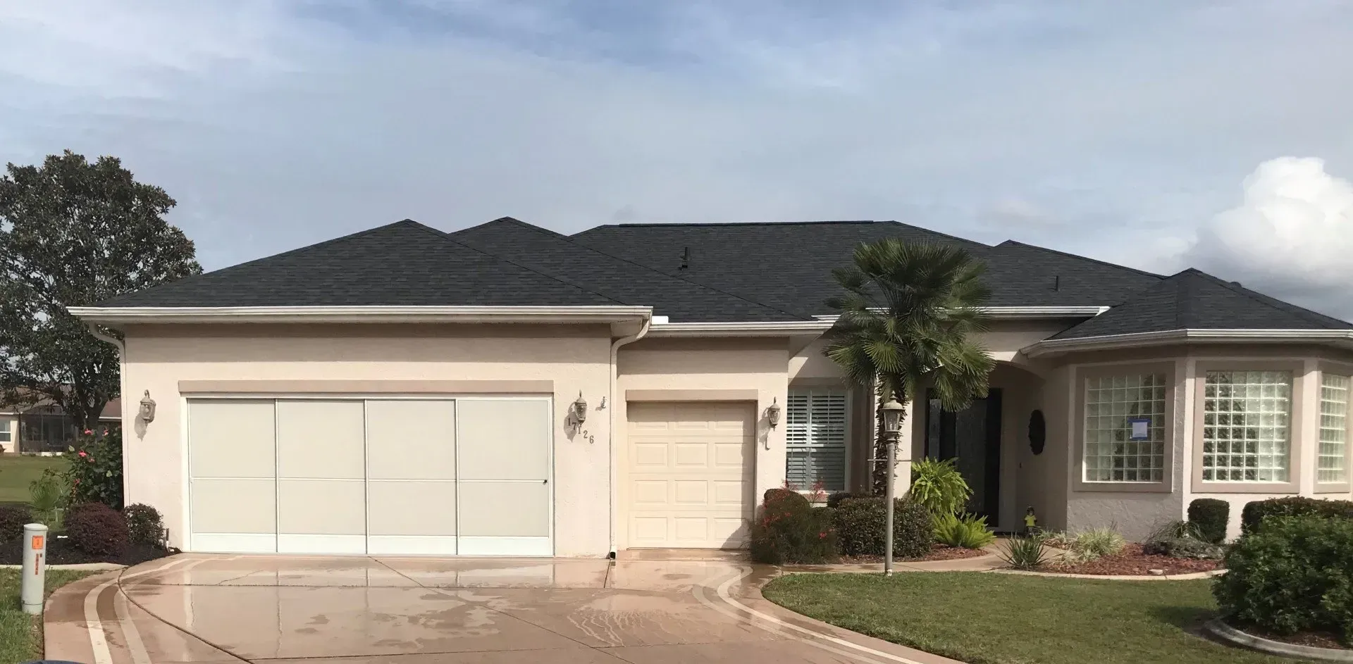 Single-story beige suburban house with a two-car garage and tiled roof, viewed from the street