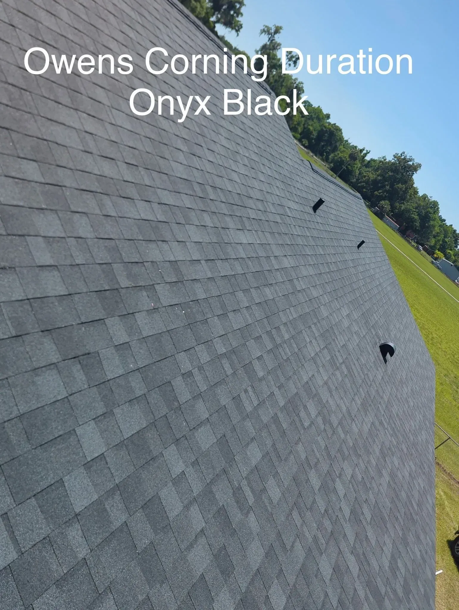 Gray roof shingles labeled “Owens Corning Duration Onyx Black” on a sloped roof under a blue sky
