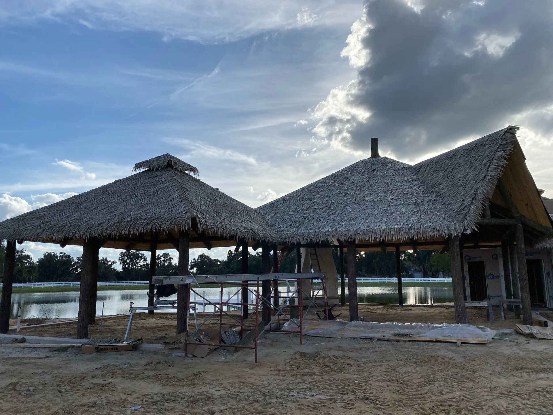 Thatched pavilion by a body of water under a cloudy sky