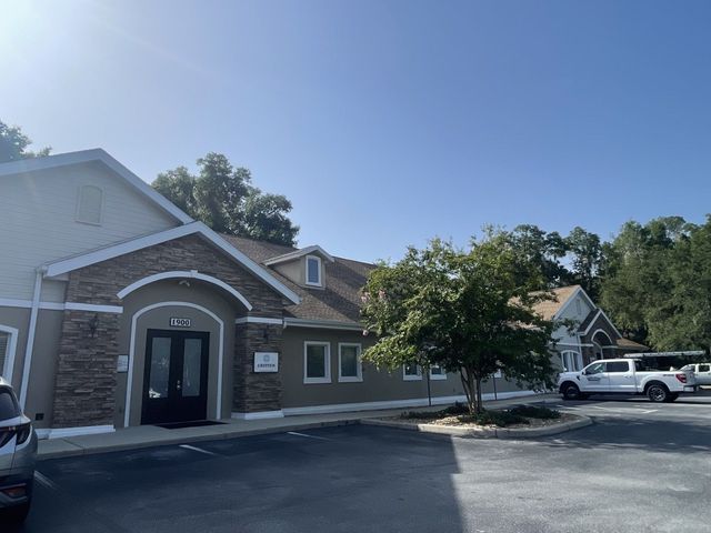Single-story suburban house with gray siding, dark roof, and a green lawn under a sunny blue sky
