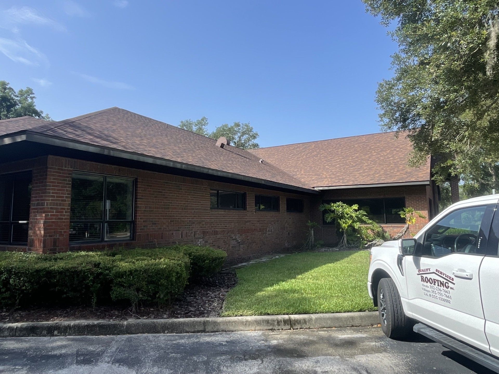 Brick house with brown roof, hedges, and a white pickup truck in the driveway under a blue sky