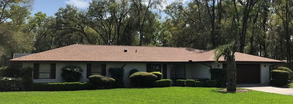 Single-story house with a red roof and manicured lawn, surrounded by trees under a bright sky