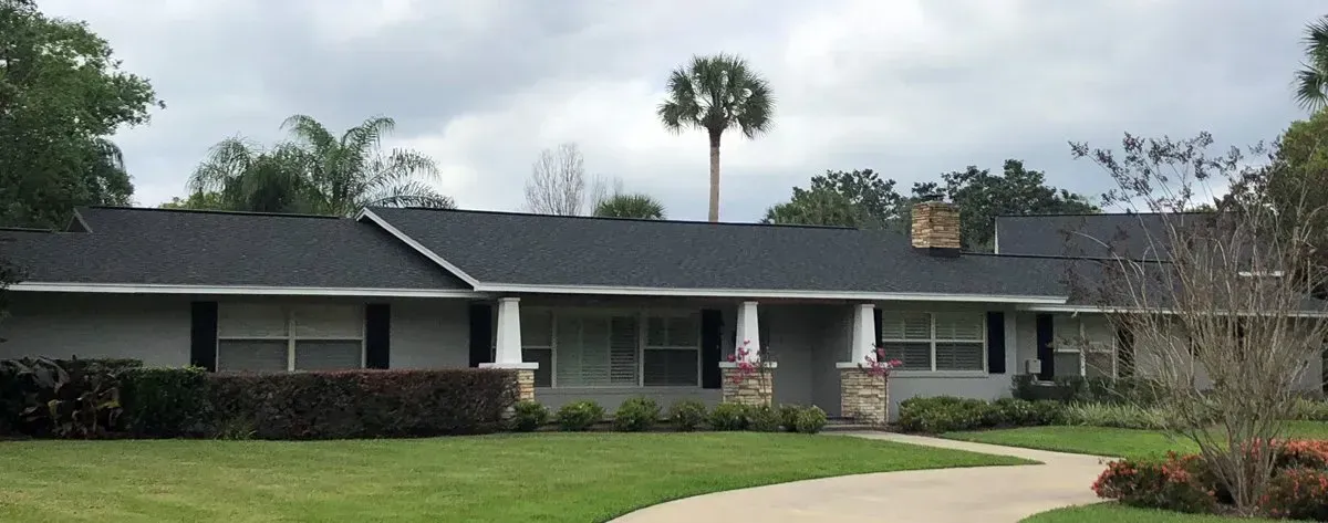 Single-story house with a dark roof, white columns, and a curved walkway in front.