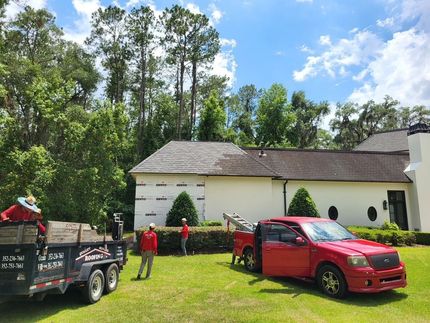 Red car and utility trailer in front of a white house with people on a grassy yard