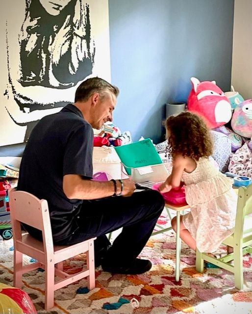 Man and child seated at small tables, looking at papers in a colorful room.