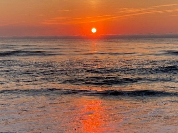 Orange sunset over ocean waves, reflecting the sun's glow.
