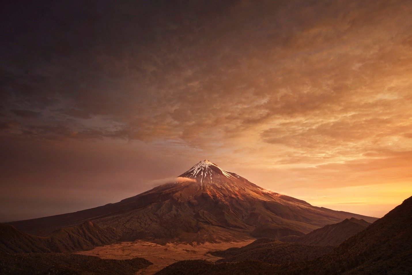Volcanic mountain under an orange and dark sky at sunset.