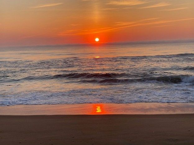 Sunrise over the ocean, with orange sun reflected on water and wet sand.