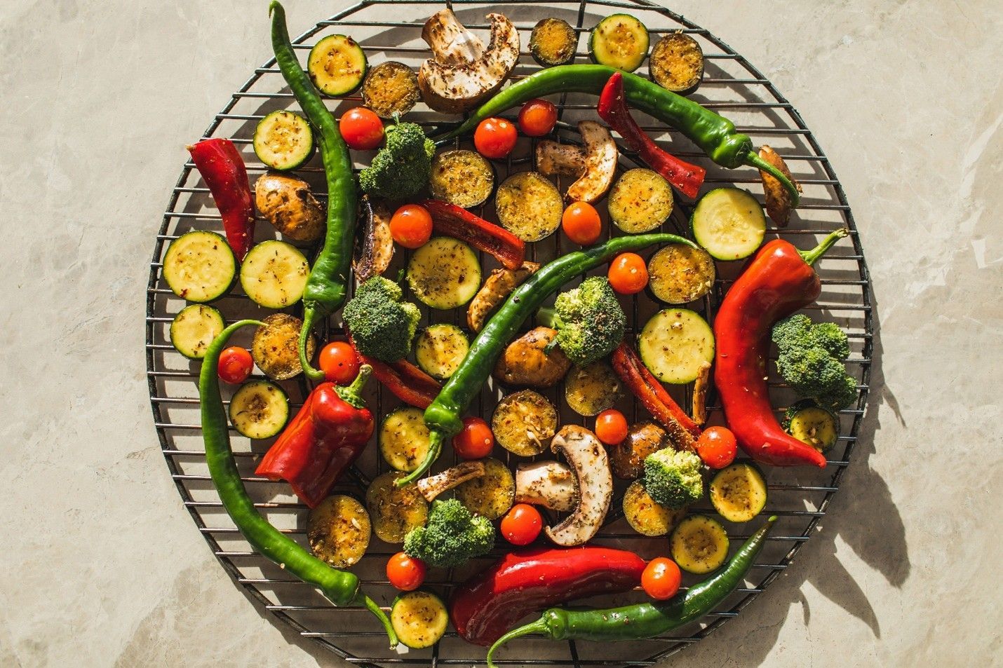 Grilled vegetables on a round grill: zucchini, peppers, broccoli, tomatoes, and mushrooms.