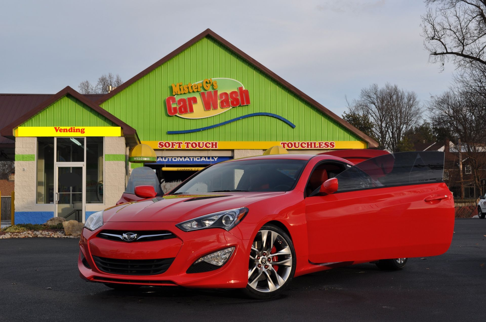 A bright red Hyundai Genesis Coupe parked in front of a green and yellow building labeled Mike's Car Wash.
