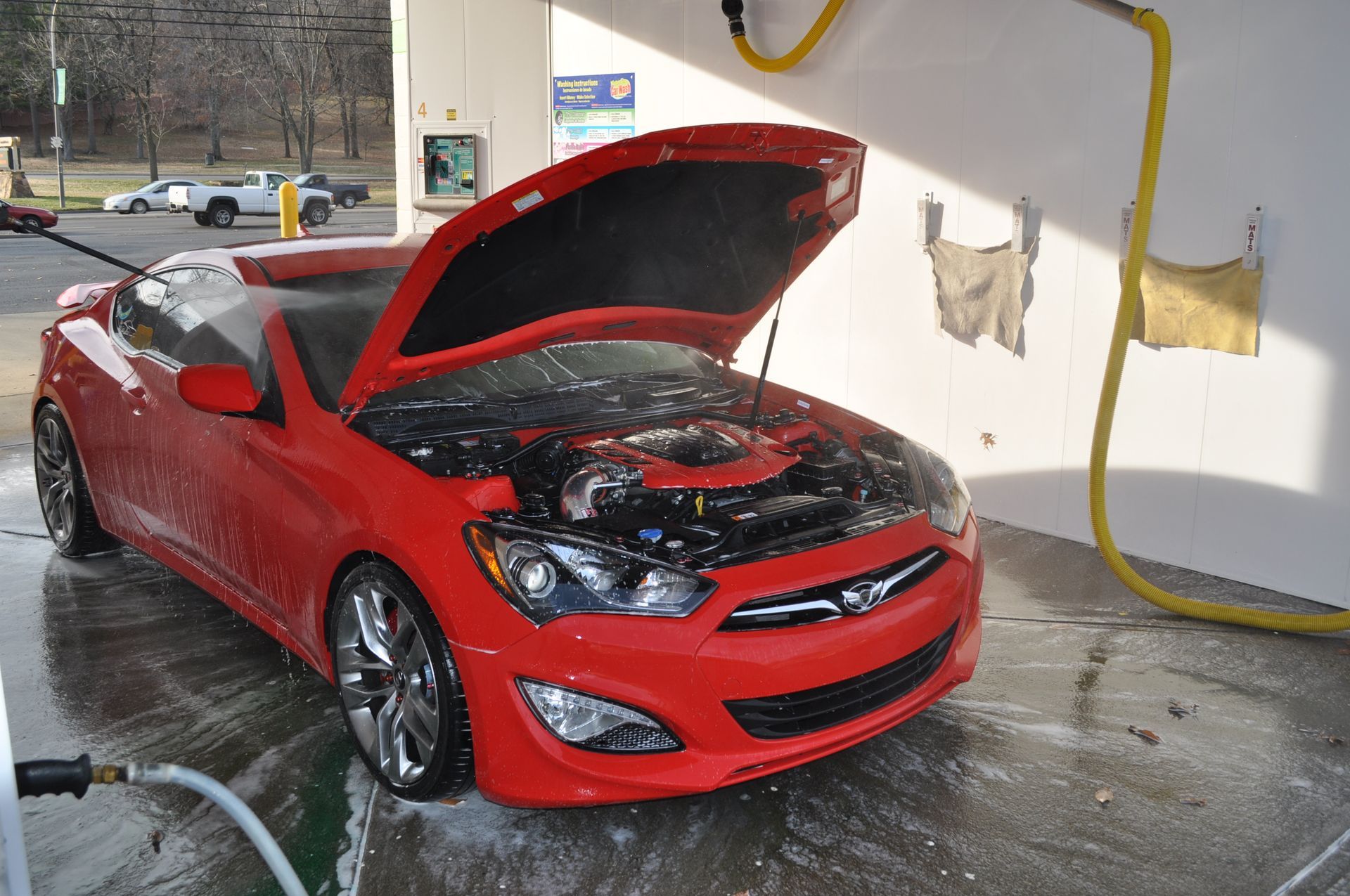 A bright red sports car with its hood open being washed in a self-service car wash bay.