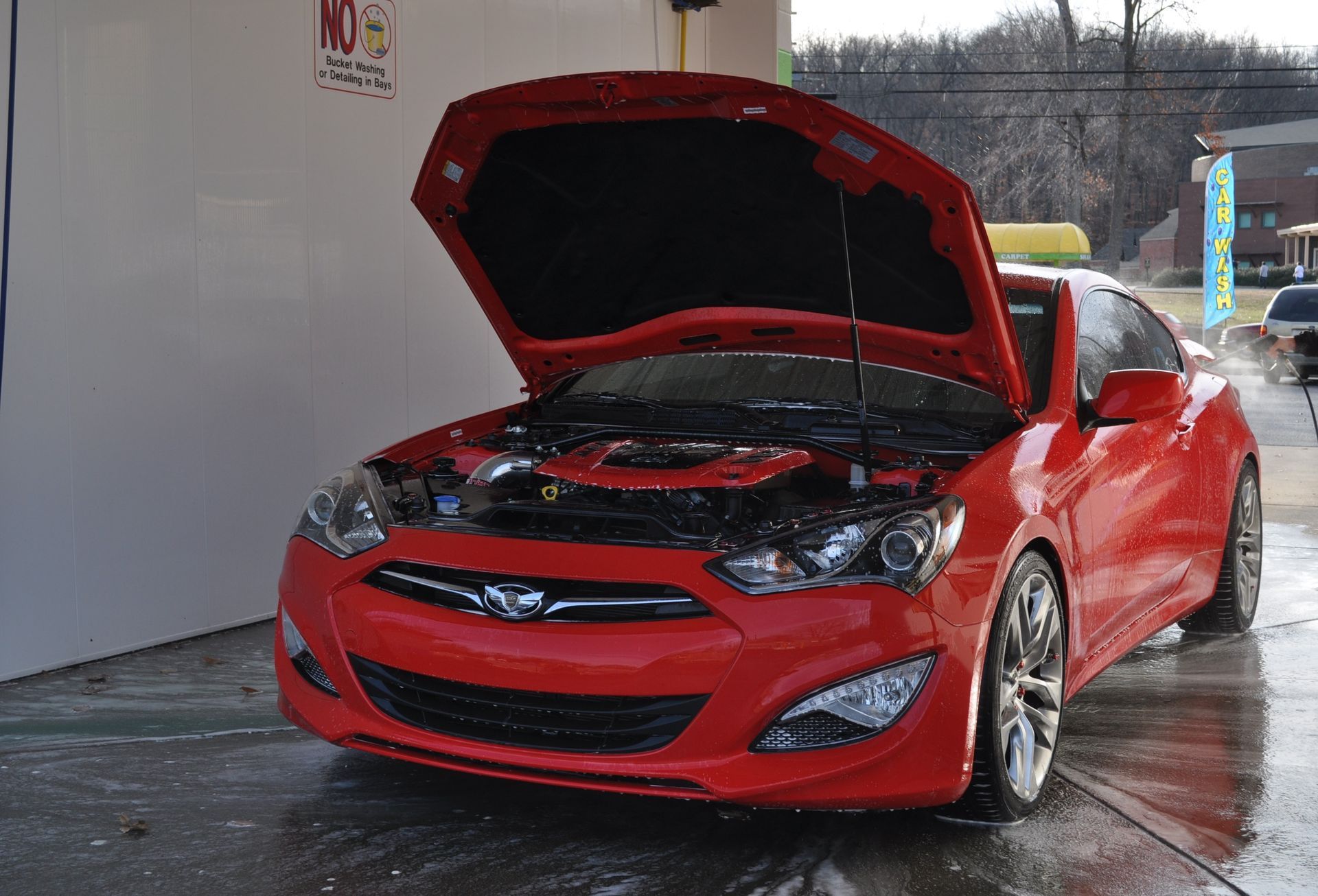 A bright red Hyundai Genesis Coupe with its hood open, parked in a car wash bay.