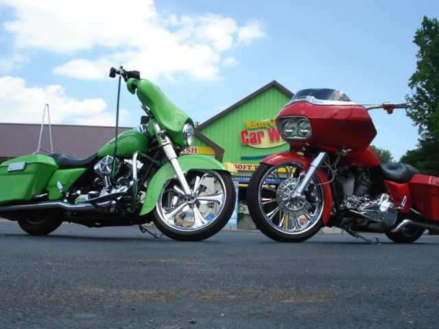 A bright green motorcycle and a red motorcycle parked side-by-side in front of a car wash building under a blue sky.