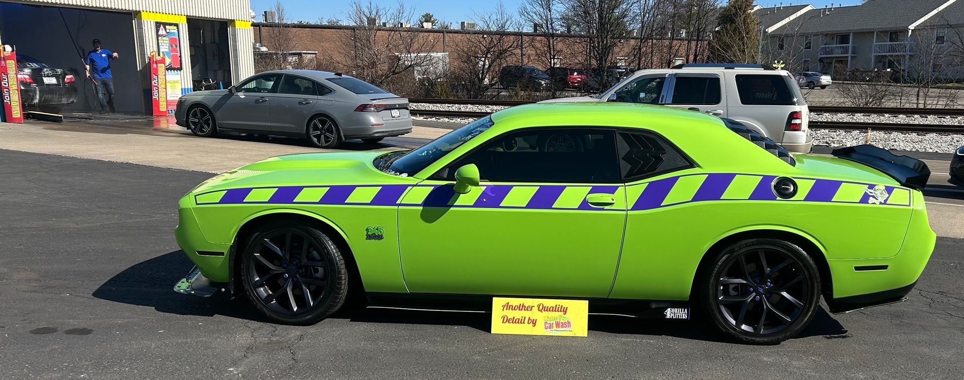 A bright green Dodge Challenger with purple racing stripes parked in a sunny lot.