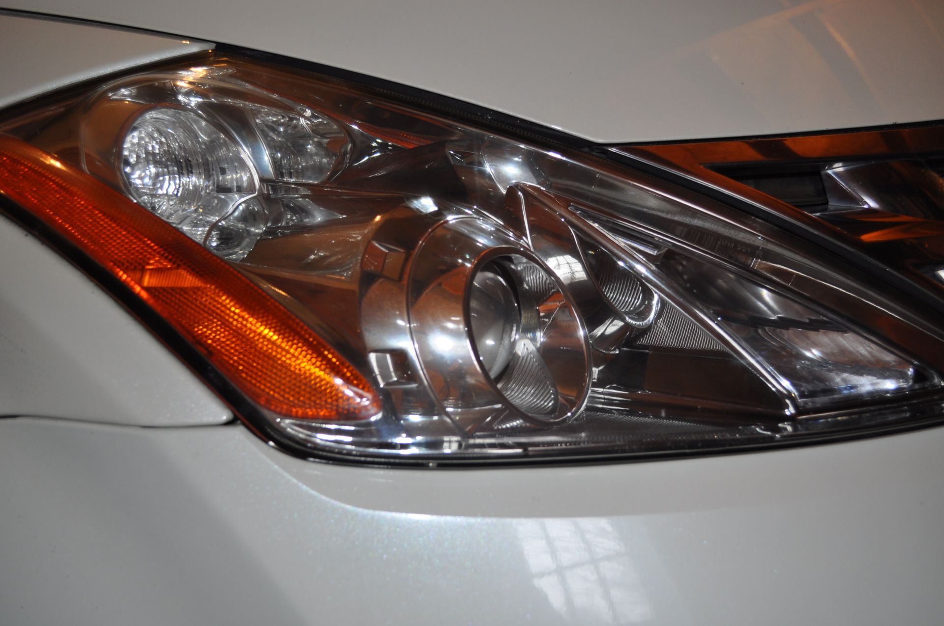 Close-up of a white car’s headlight assembly, featuring a clear lens, a round projector bulb, and an orange side marker.