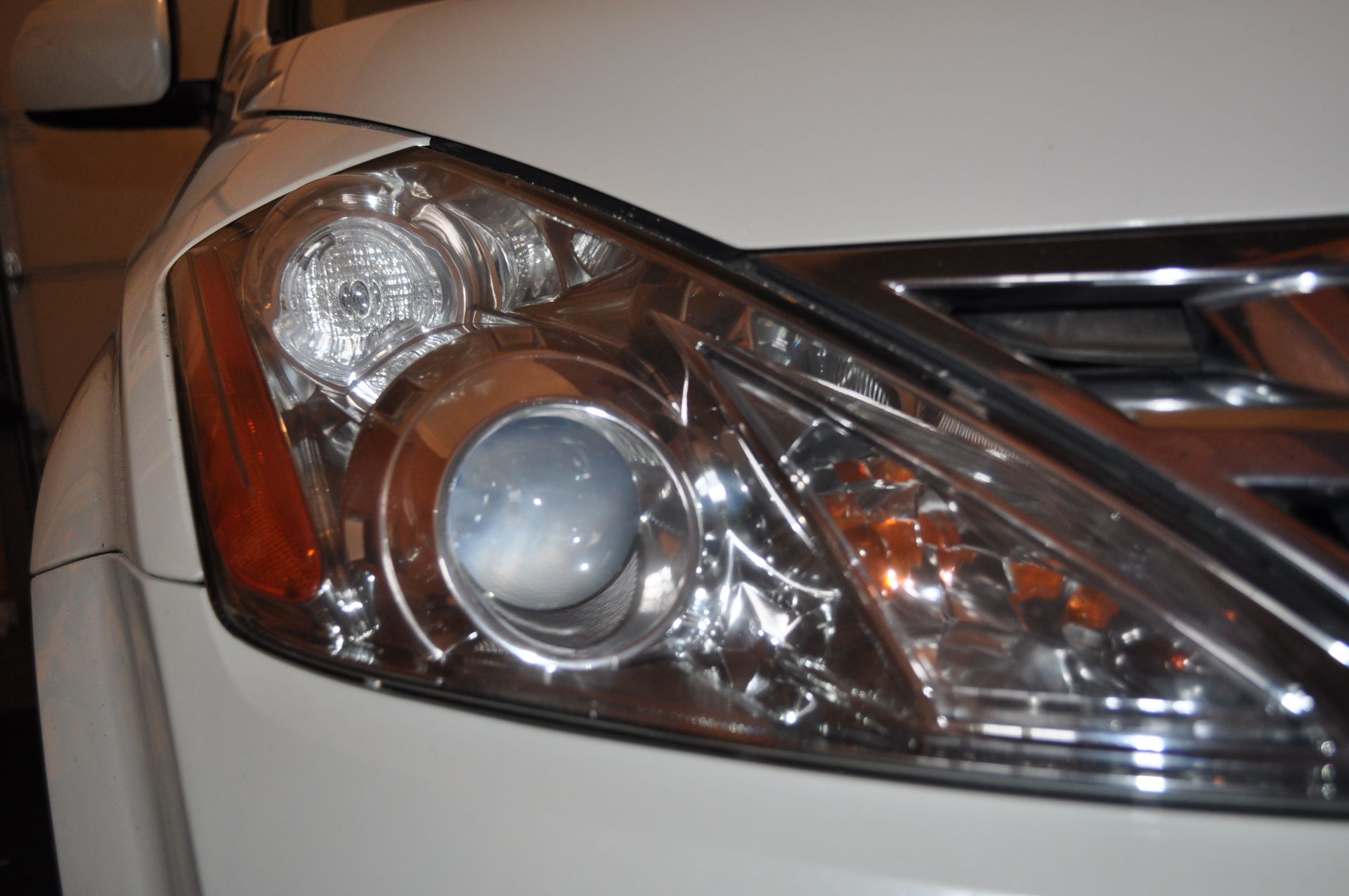 Close-up of a white car's headlight assembly featuring a clear projector lens, chrome housing, and amber side light.