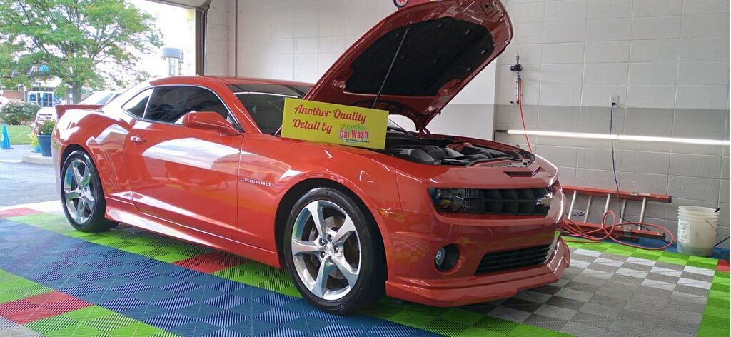 An orange Chevrolet Camaro with its hood open, parked indoors on a colorful, tiled floor.