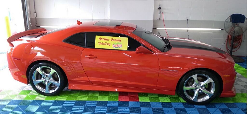 A vibrant red Chevrolet Camaro with black racing stripes and chrome wheels parked inside a garage on tiled flooring.