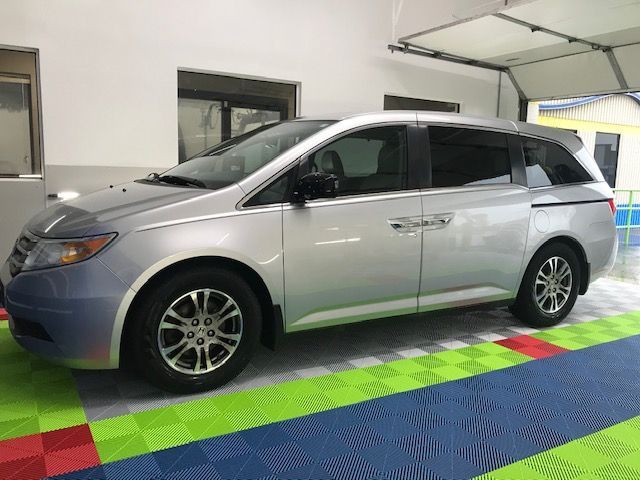 Silver minivan parked inside a garage with a green, blue, and red checkered floor.