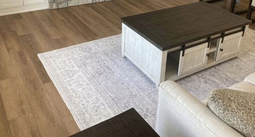 Modern living room with a white rug, dark coffee table, and beige sofa on wood flooring