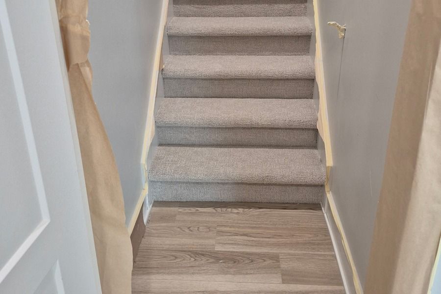 Narrow indoor stairway with gray carpeted steps and beige walls, viewed from the bottom up