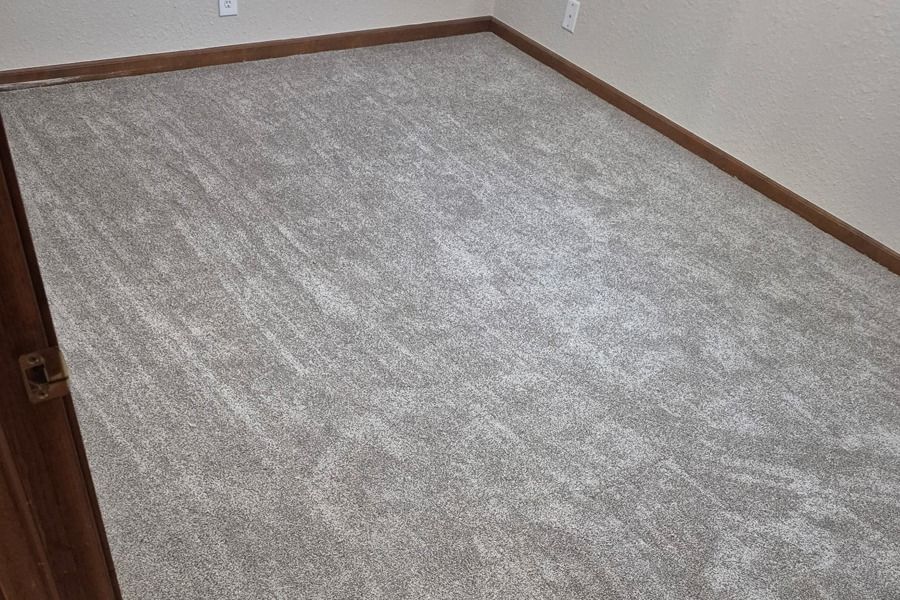 Empty beige carpeted room with brown baseboards and a partially visible wooden door.