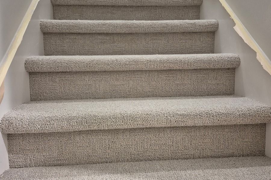 Carpeted indoor staircase with light beige steps and white walls