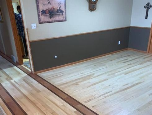 Empty room with newly finished light wood floors, dark wainscoting, wall decor, and an open doorway