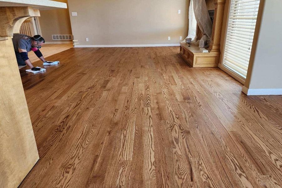 Spacious living room with hardwood floors and large windows; person working near the far wall.