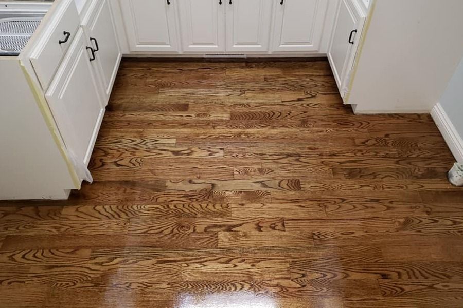 Empty kitchen with glossy hardwood floor and white cabinets and drawers.