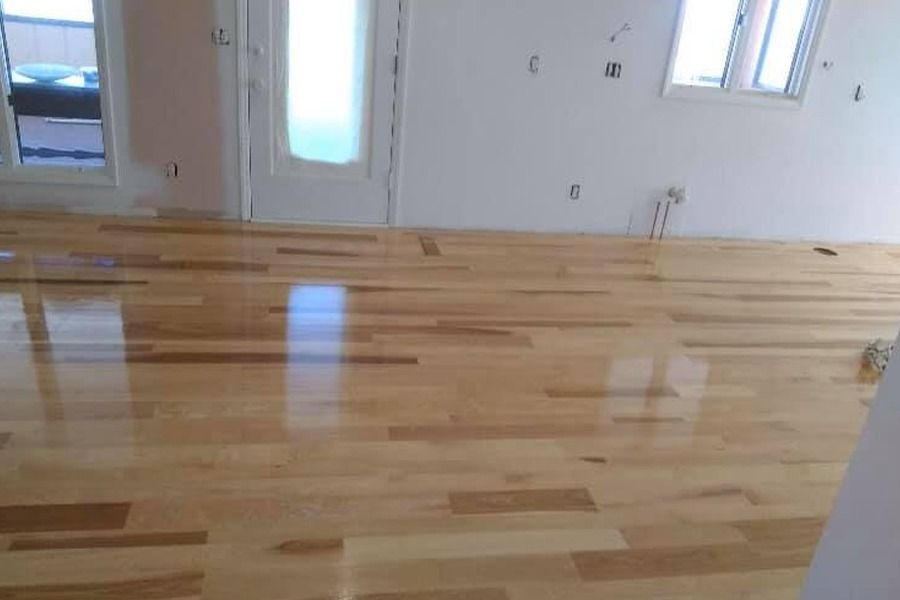 Empty room with glossy hardwood floor and white walls, with windows and a door in the background