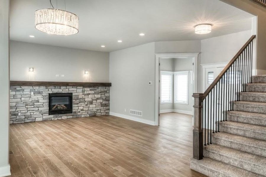Bright living room with hardwood floors, stone fireplace, recessed lights, and carpeted staircase.