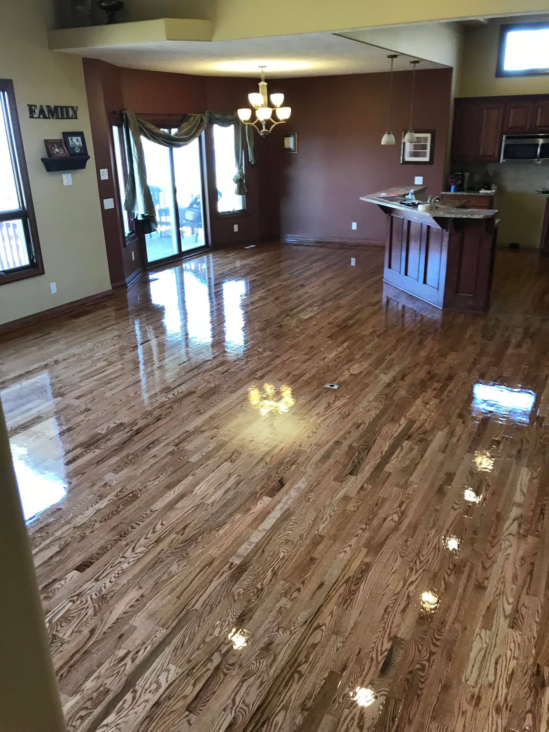 Empty polished living room with glossy wood floors, chandelier, and a kitchen counter in the background