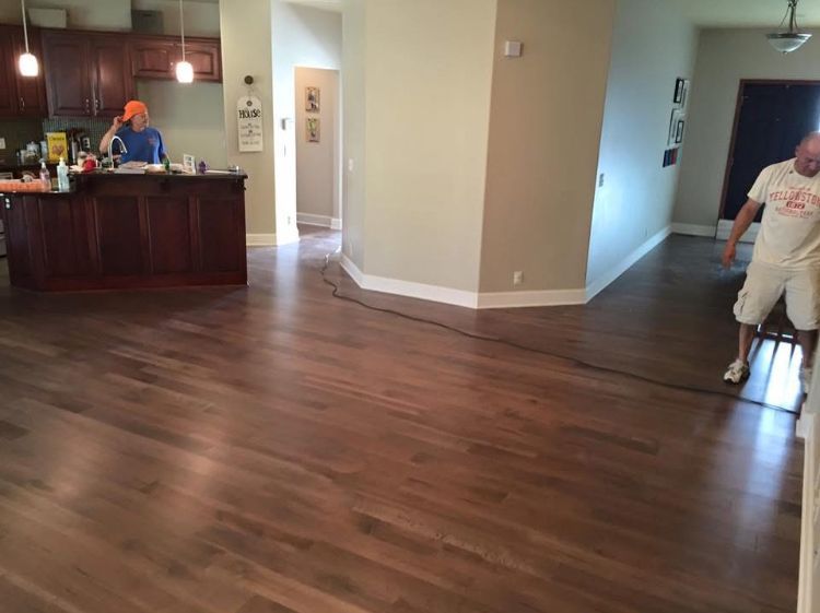 Empty living room with hardwood floors, kitchen in background, and a person standing near the doorway.