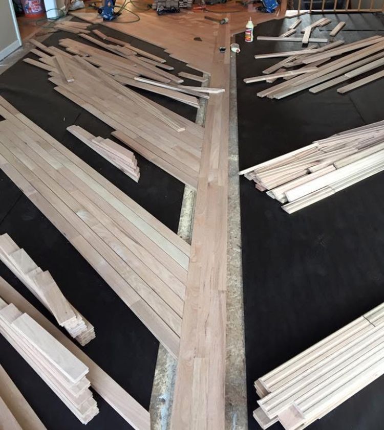 Stacks of light-colored wood planks arranged in rows on a dark floor, like a workshop or warehouse.