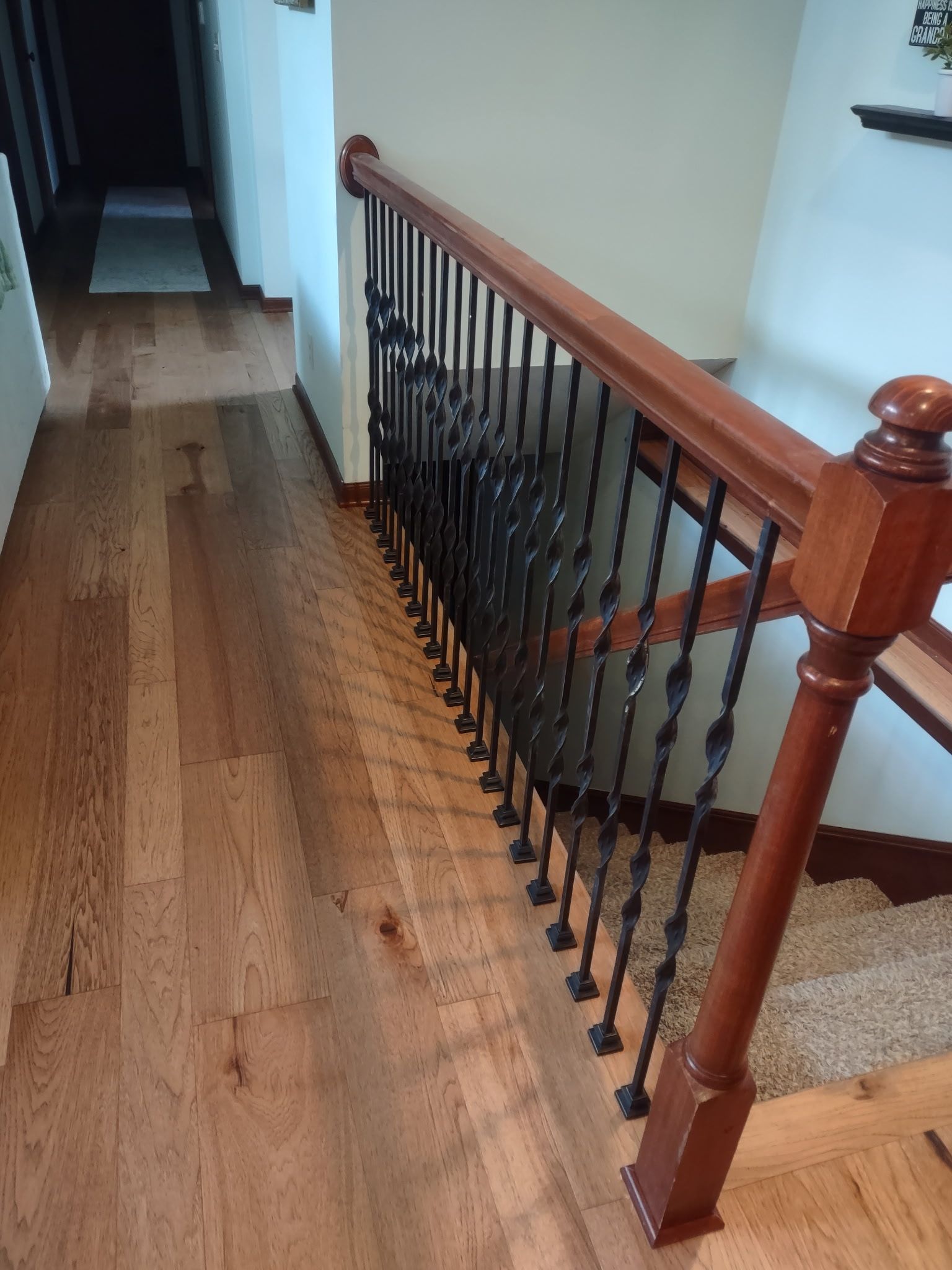 Wooden upstairs hallway with a dark metal-and-wood stair railing and carpeted stairs below.