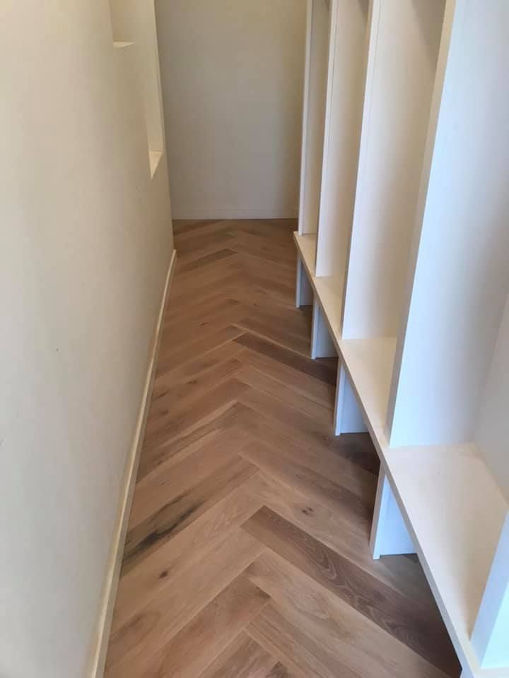 Narrow hallway with light walls, herringbone wood floor, and built-in white shelving on the right