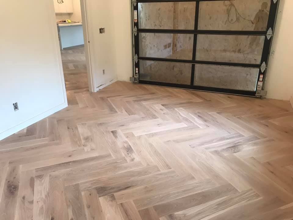 Empty room with light wood herringbone floor and a garage door in the background