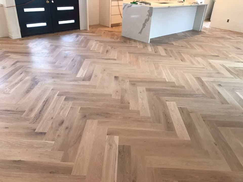 Empty room with light herringbone wood flooring and a white desk near a black door.