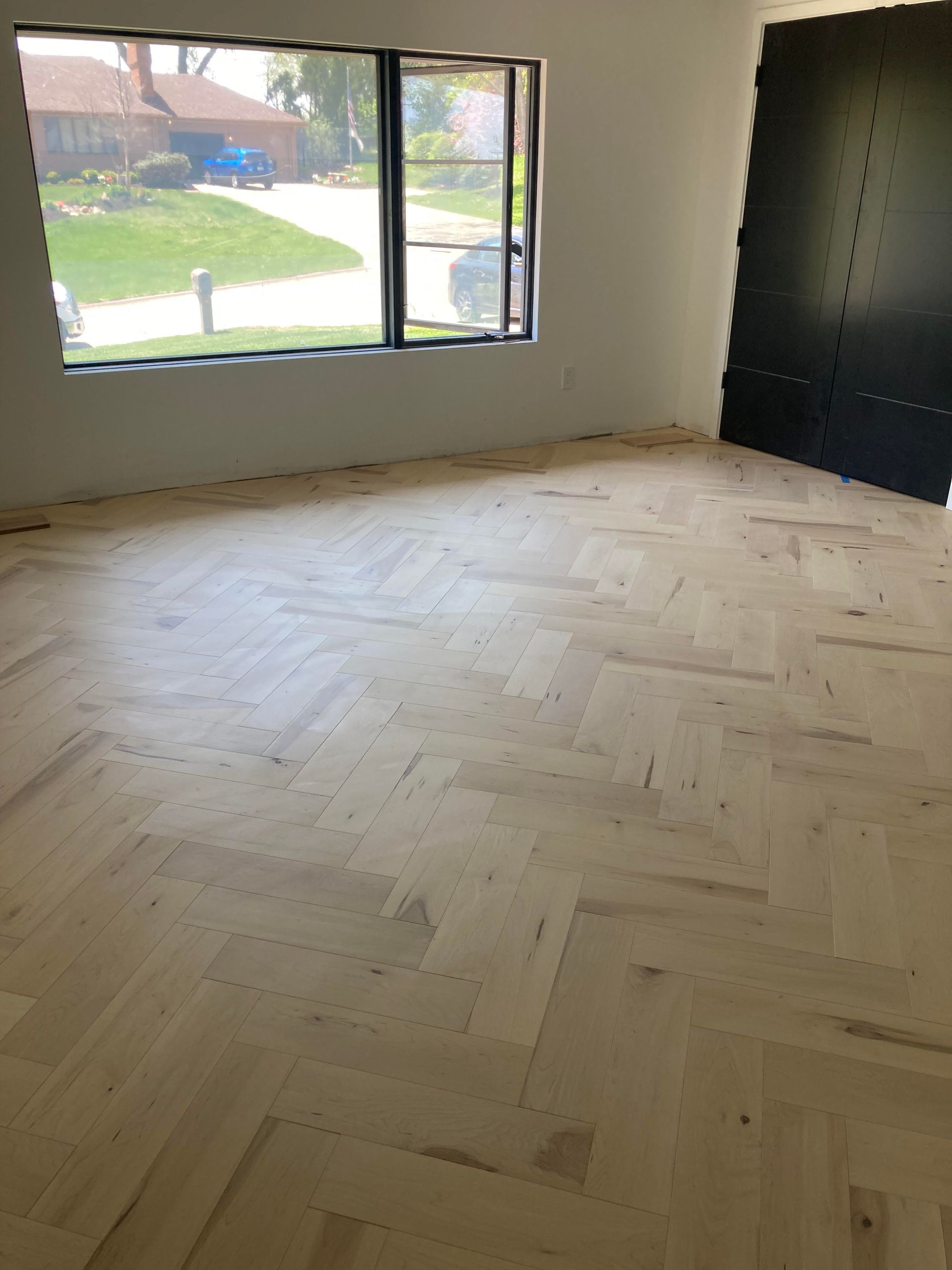 Empty room with herringbone wood floor, large window, and black built-in storage wall