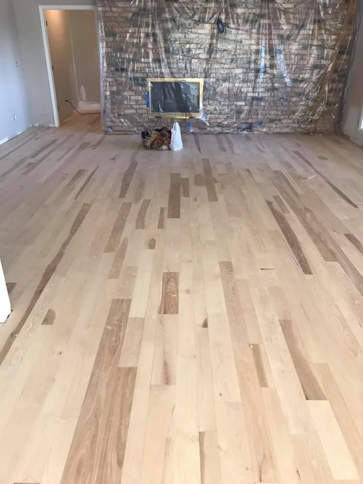 Empty room with light wood floors, a stone fireplace, and foil-covered wall panels