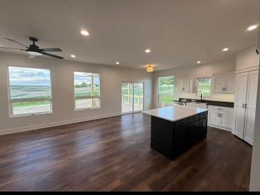 Spacious modern kitchen with dark wood floors, white cabinets, an island, and large windows overlooking a green view