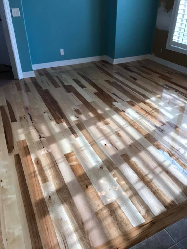 Empty room with teal walls and a newly installed striped wood floor in sunlight.