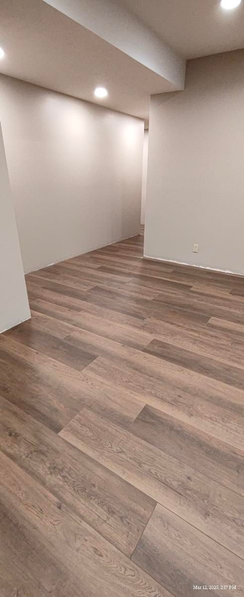 Empty modern room with wood-look flooring, white walls, and recessed ceiling lights